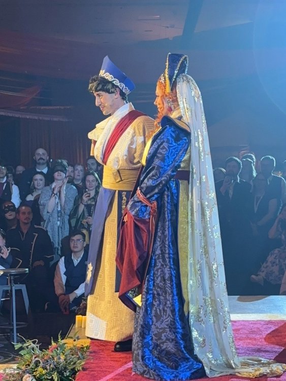 Actors dressed as Shallan and Adolin in their wedding regalia stand on a stage in front of dressed up fans