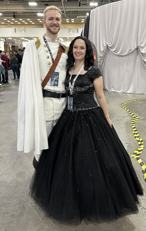 A couple dressed as Vin and Elend from Misborn in their full ball regalia - Elend in a white uniform and Vin in a black ball gown