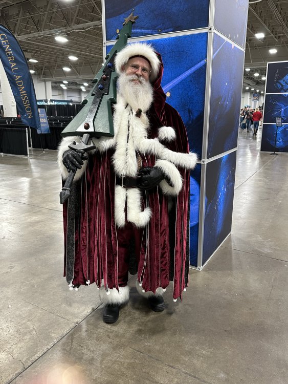 Mistborn Santa posing in the convention hall with christmas tree shardblade resting on his shoulder