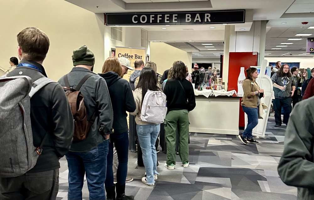 a line of people wearing backpacks standing in line at a coffee bar in the convention center