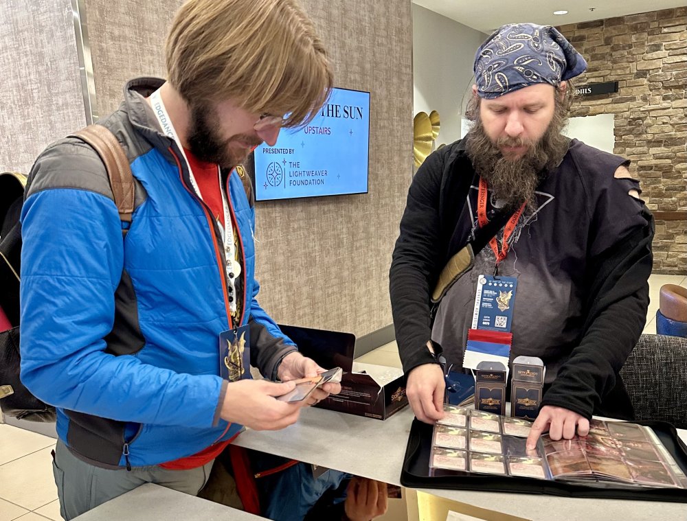 two people at a table trading cards, one with cards in their hands and the other with a binder of cards in a glossy sleeve protector